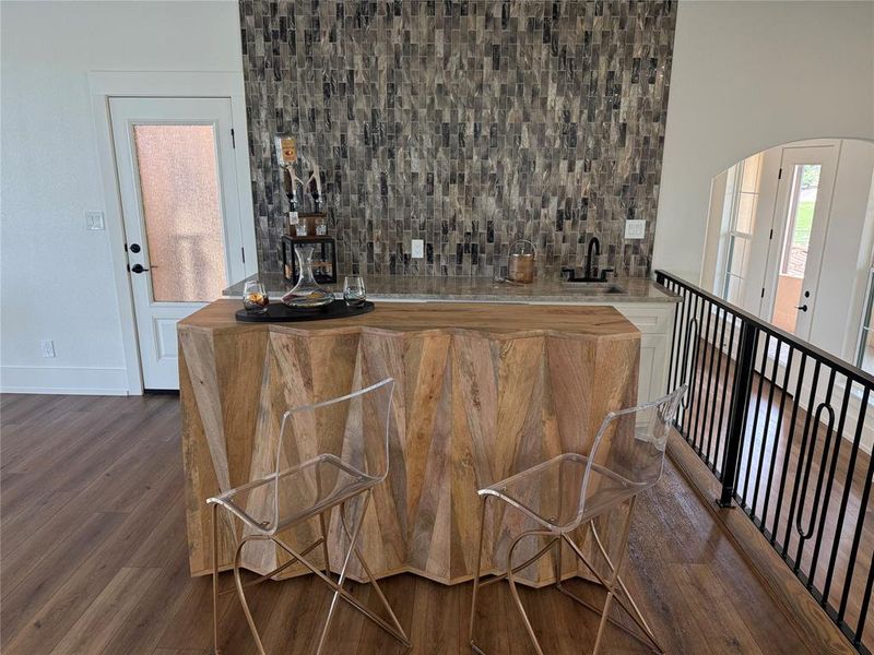 Indoor wet bar featuring tasteful backsplash, wood finished floors, and arched walkways Indoor wet bar featuring tasteful backsplash, wood finished floors, and arched walkways