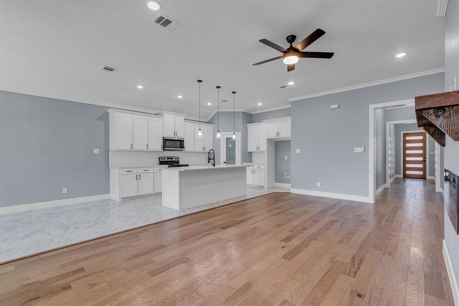 Unfurnished living room featuring sink, ornamental molding, ceiling fan, and light wood-type flooring