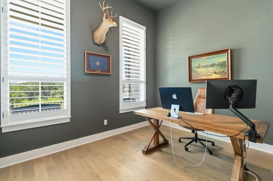 An inviting home office boasts rich hardwood flooring and large windows, offering inspiring views.