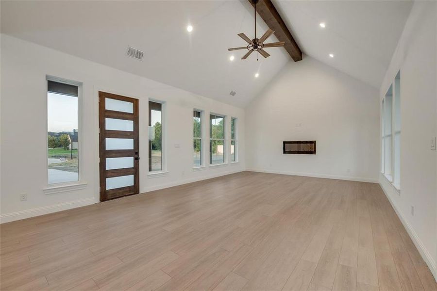 Unfurnished living room with beam ceiling, high vaulted ceiling, light wood-style floors, recessed lighting, and a glass covered fireplace