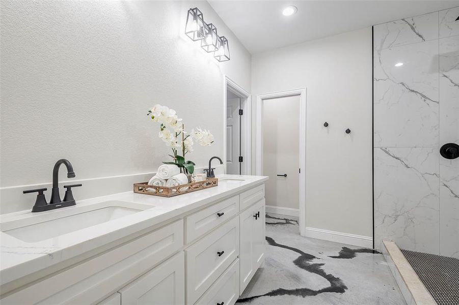 Bathroom with dual vanity, a tile shower, and concrete flooring