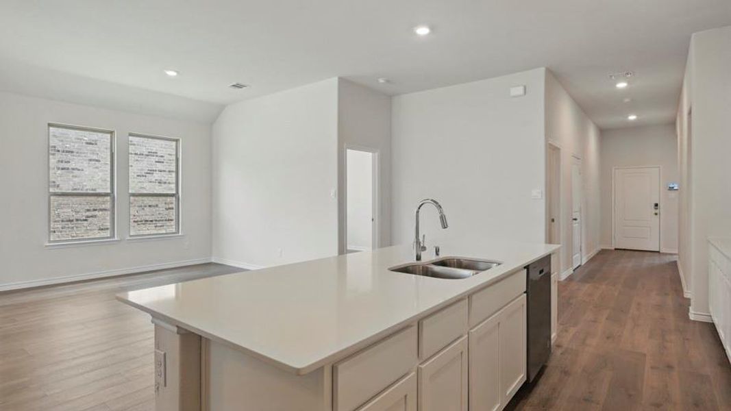 Kitchen island featuring a double-basin stainless steel sink, gooseneck faucet, light-toned countertop, and integrated dishwasher