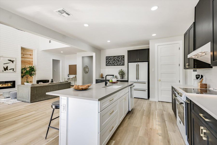 Kitchen featuring a breakfast bar area, open floor plan, light wood-style flooring, white appliances, and white cabinets