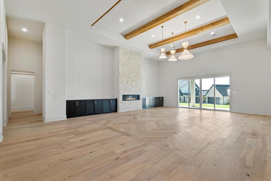 Unfurnished living room with a towering ceiling, beamed ceiling, recessed lighting, a stone fireplace, and light wood finished floors