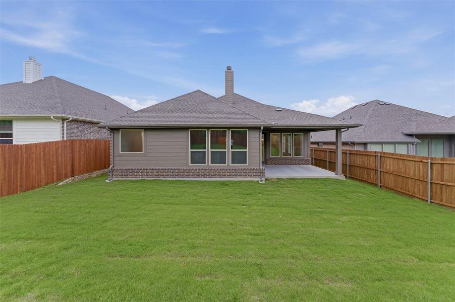Expansive backyard featuring a manicured lawn, wood fencing, and a concrete patio with an overhead roof extension
