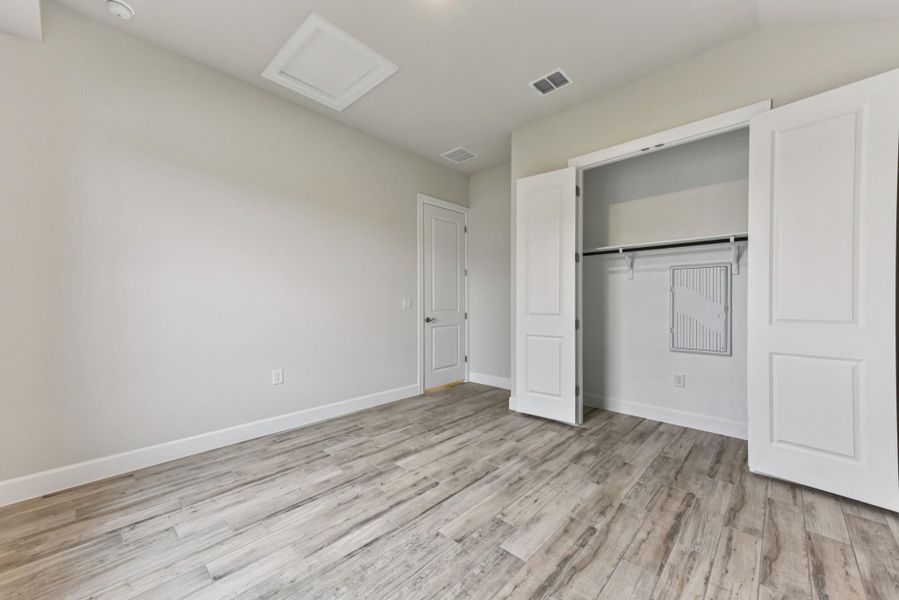 Unfurnished bedroom with attic access, light wood-style flooring, and a closet