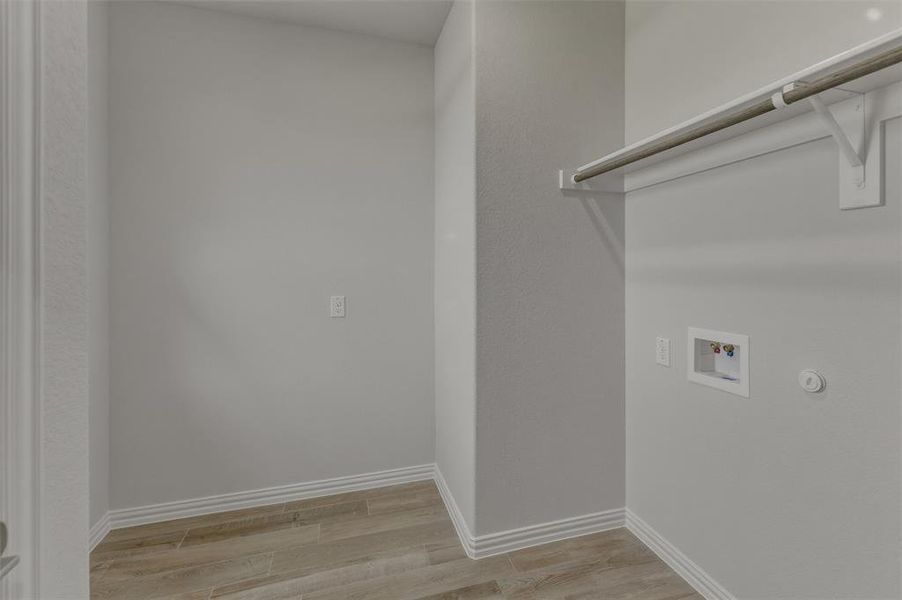 Dedicated utility space featuring wood-finish flooring, light gray walls, white baseboards, and a built-in hanging rod