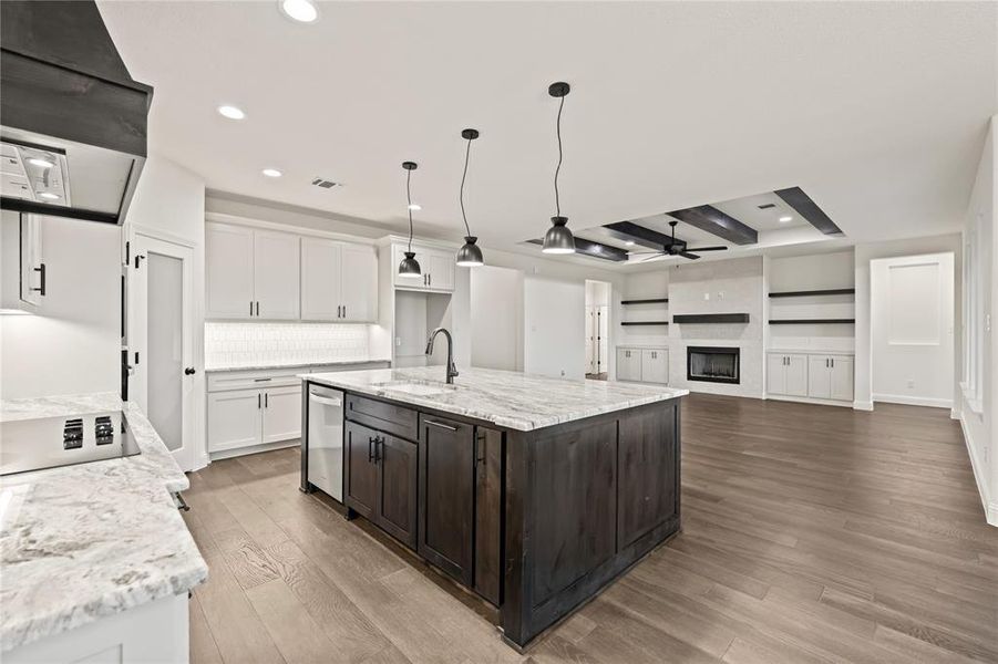 Kitchen featuring ventilation hood, light stone countertops, pendant lighting, white cabinets, and a fireplace