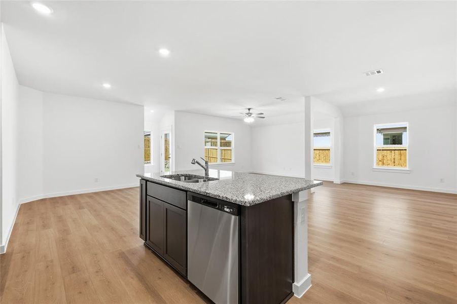 Kitchen with open floor plan, dishwasher, a center island with sink, light stone counters, and recessed lighting