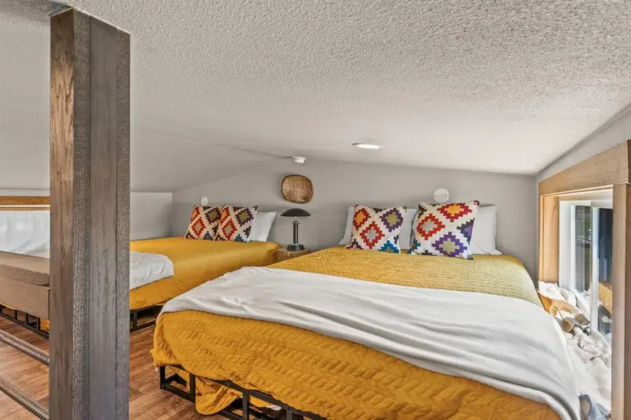 Bedroom featuring vaulted ceiling, a textured ceiling, and wood finished floors