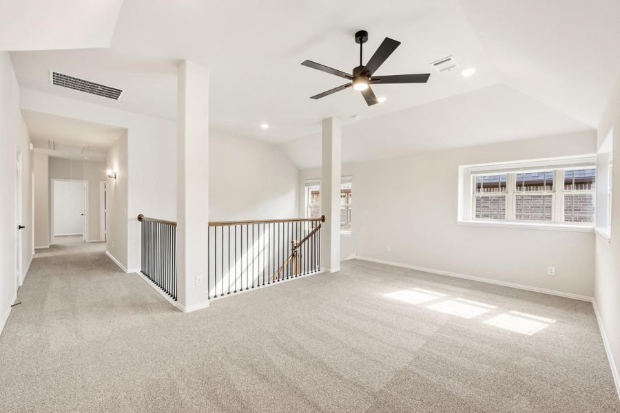Open upstairs loft with carpet, ceiling fan, iron stair railing, and hallway leading to bedrooms