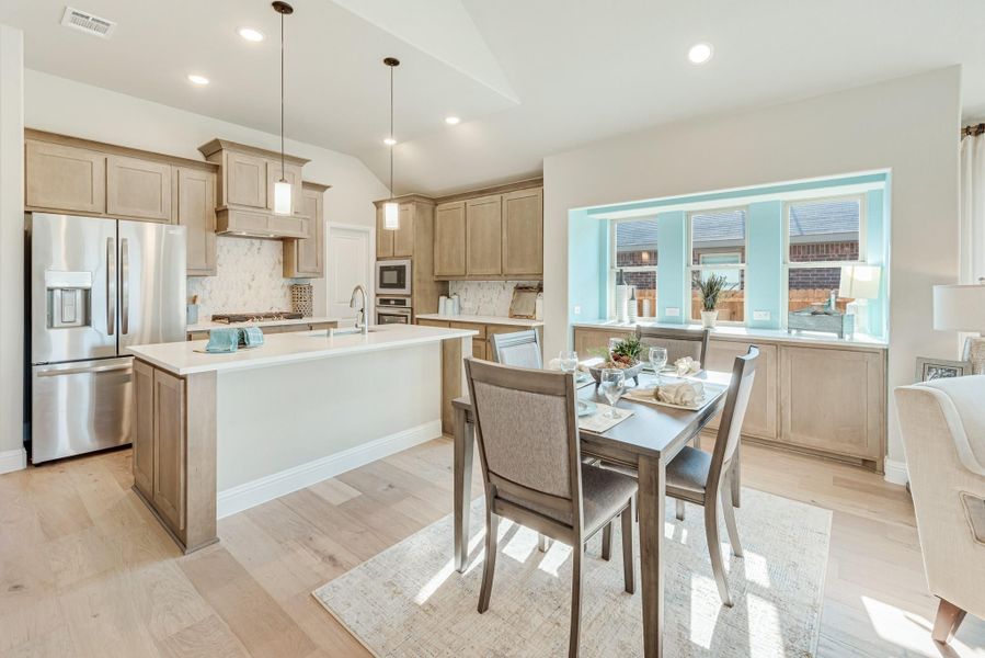 Open kitchen and dining area with light wood cabinets, center island, stainless appliances, and hardwood floors