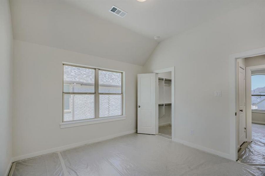 Vaulted ceiling bedroom featuring a large double window, a walk-in closet with shelving, and light-toned walls