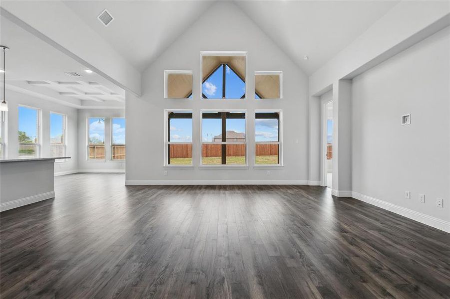 Unfurnished living room featuring dark wood-style flooring, high vaulted ceiling, baseboards, and visible vents