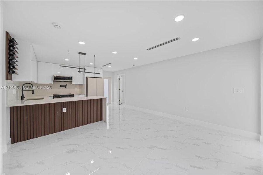 Kitchen island with vertical slat wood-finish paneling, white shaker-style cabinetry, a built-in wine rack, and a linear pendant light fixture Kitchen island with vertical slat wood-finish paneling, white shaker-style cabinetry, a built-in wine rack, and a linear pendant light fixture