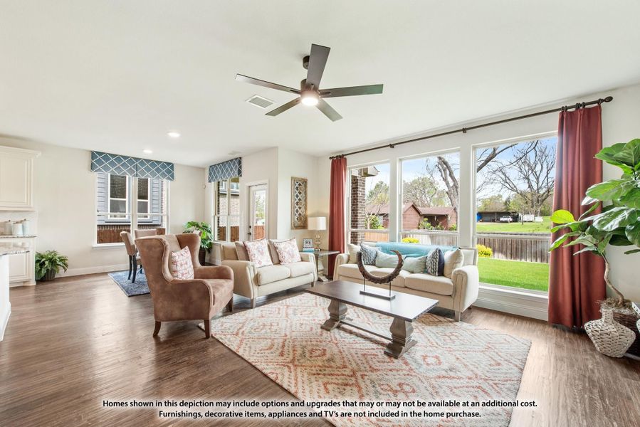 Bright living room with hardwood floors, ceiling fan, large windows, and seating area overlooking backyard