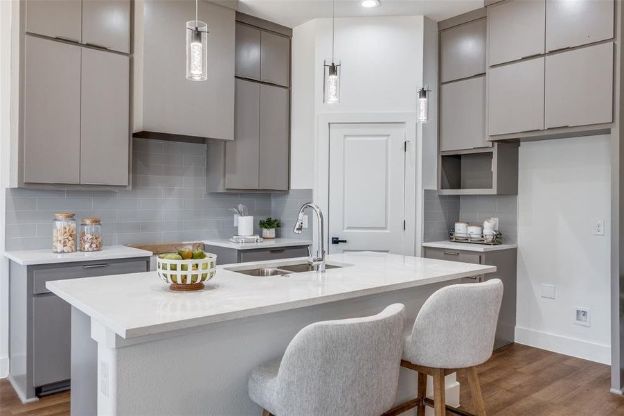 Kitchen with a kitchen island with sink, wood-type flooring, pendant lighting, sink, and tasteful backsplash