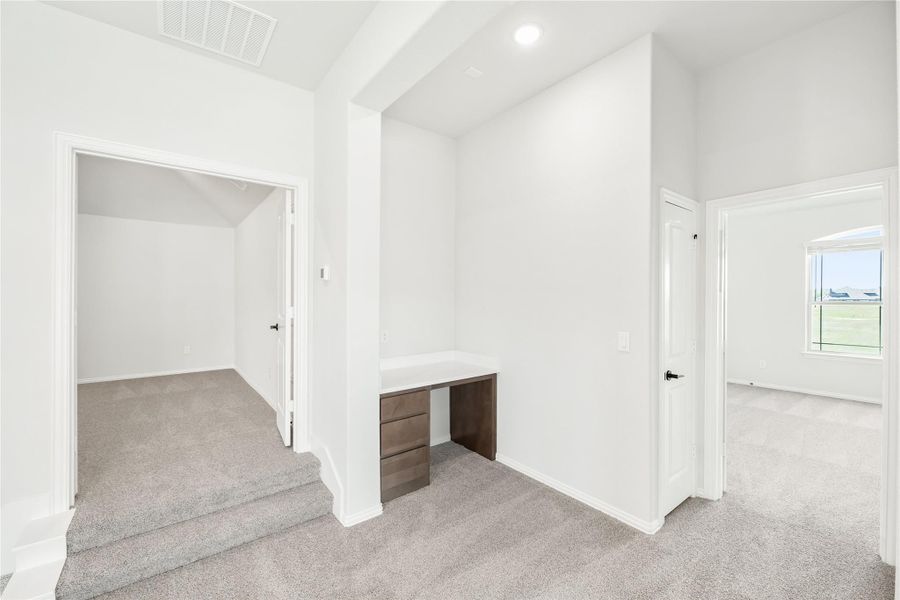 Upstairs hallway with built-in desk, gray carpet, and open doors to adjacent rooms