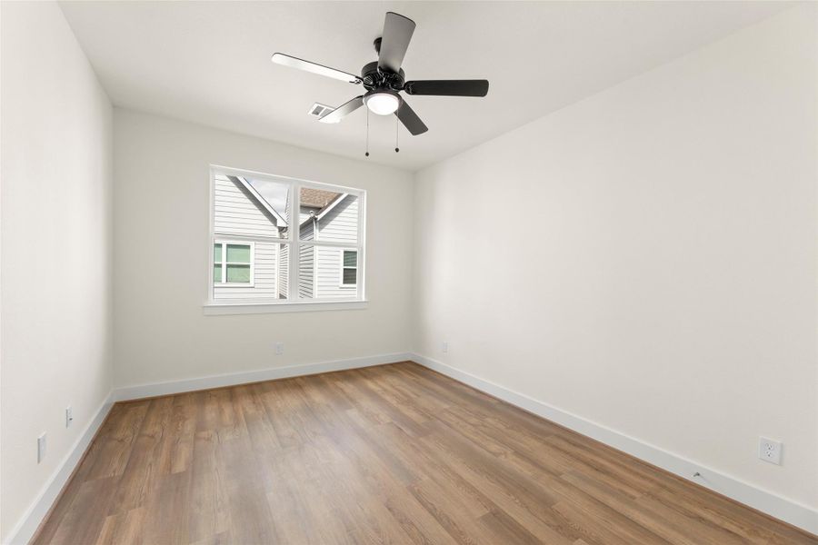 This room features a sleek ceiling fan, light walls, and a window providing natural light. The flooring adds warmth, making it a bright and inviting space.