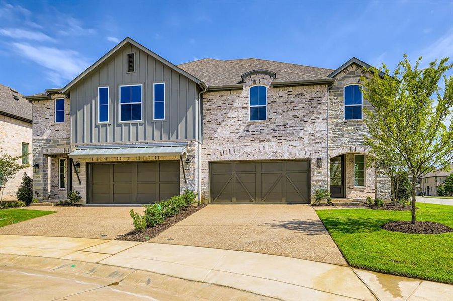 View of front of property with board and batten siding, driveway, an attached garage, and a front lawn