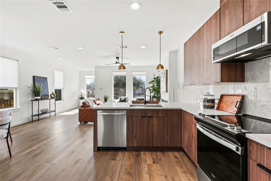 Kitchen with kitchen peninsula, appliances with stainless steel finishes, ceiling fan, sink, and dark hardwood / wood-style floors