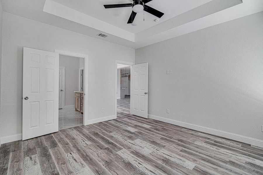 Unfurnished bedroom with ensuite bathroom, wood-type flooring, and a raised ceiling