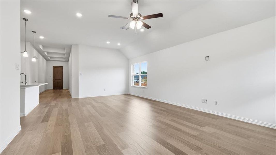 Spacious living area featuring light wood-finish flooring, vaulted ceilings, and recessed lighting Spacious living area featuring light wood-finish flooring, vaulted ceilings, and recessed lighting