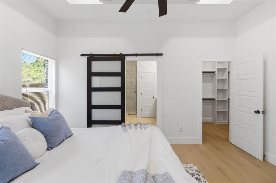 Vaulted ceiling featuring a ceiling fan, light wood-finish flooring, a sliding barn door with frosted glass panels, and an organized closet with shelving and hanging rods