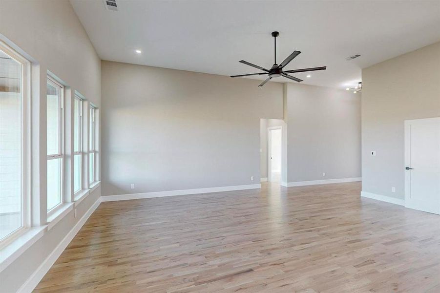 Empty room with light hardwood / wood-style floors, a towering ceiling, a wealth of natural light, and ceiling fan