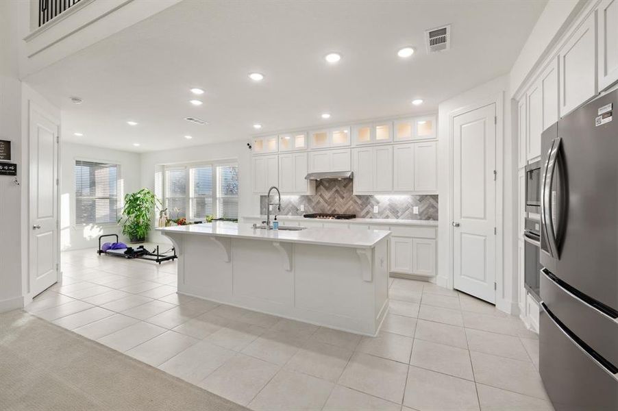 Kitchen with appliances with stainless steel finishes, glass insert cabinets, white cabinetry, a kitchen breakfast bar, and light tile patterned floors