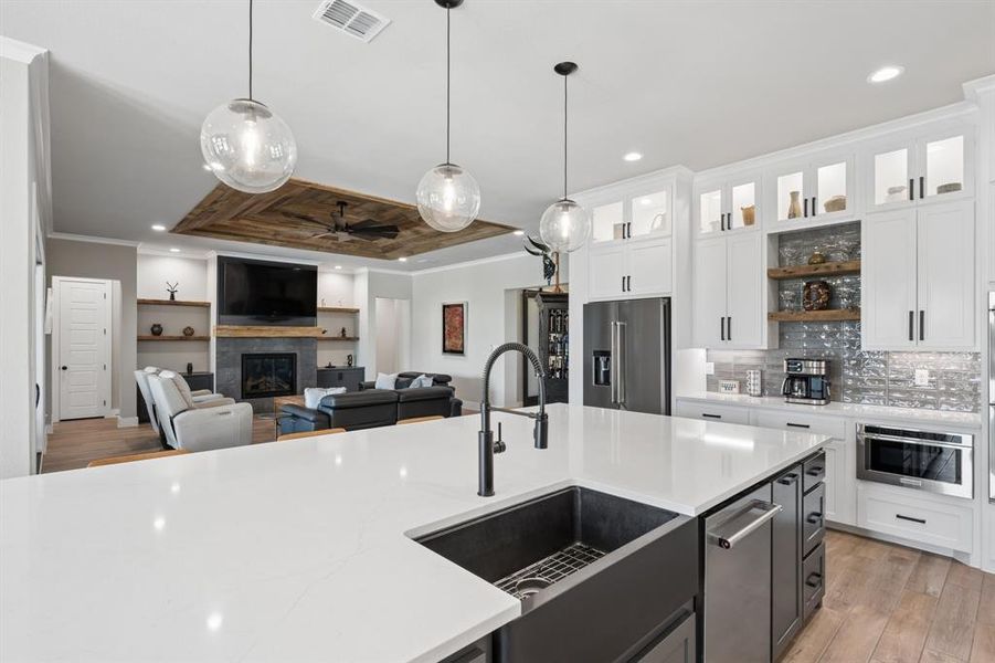 Kitchen with two tone cabinetry, crown molding, open floor plan, light wood finished floors, and a fireplace