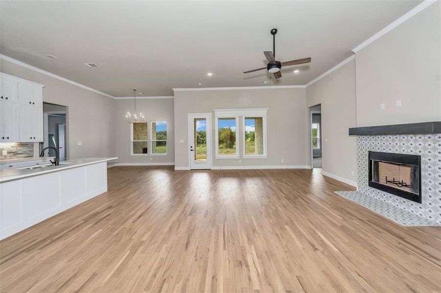 Unfurnished living room with light hardwood / wood-style flooring, ceiling fan with notable chandelier, a fireplace, sink, and ornamental molding