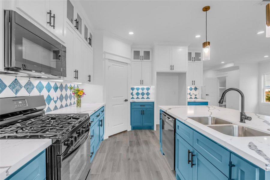 Discover the heart of your home in this stunning kitchen, featuring vibrant blue cabinetry, sleek stainless steel appliances, and elegant marble countertops, all accented by stylish geometric backsplash tiles for a perfect blend of modern flair and functionality.