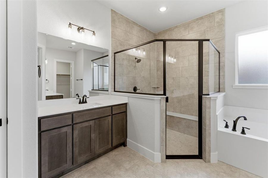 Spacious bathroom featuring a frameless glass shower enclosure with tile surround, a built-in soaking tub with dark bronze fixtures, a vanity with dark wood-finish cabinetry, a white countertop, and contemporary lighting
