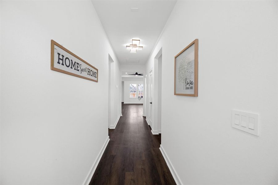 Bright, welcoming hallway with white walls and dark wood flooring. Features modern lighting and decor, leading to a room with large windows.