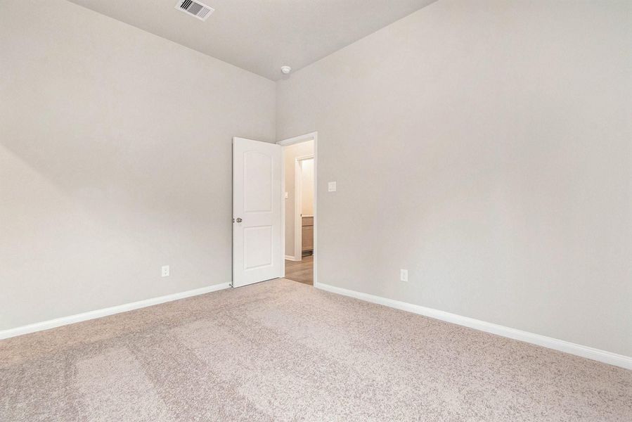 This photo shows a bright, empty room with neutral-colored walls and carpet. It features a high ceiling and an open door leading to another area, creating a spacious feel.