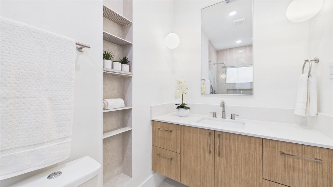 Modern bathroom with a sleek design featuring a large mirror, wooden vanity with dual sinks, and open shelving for storage. Bright and inviting with white walls and contemporary fixtures.
