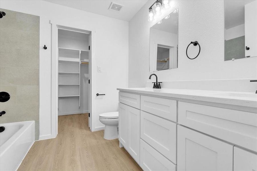 Full bathroom with toilet, hardwood / wood-style floors, tiled shower / bath combo, and vanity