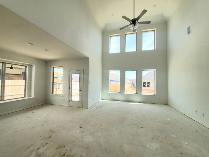 Unfurnished living room featuring concrete flooring, a ceiling fan, visible vents, and a towering ceiling