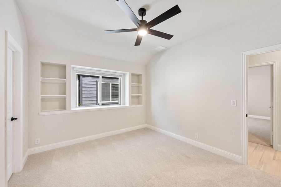 Empty bedroom with carpet, ceiling fan, built-in shelves flanking a window, and vaulted ceiling Empty bedroom with carpet, ceiling fan, built-in shelves flanking a window, and vaulted ceiling