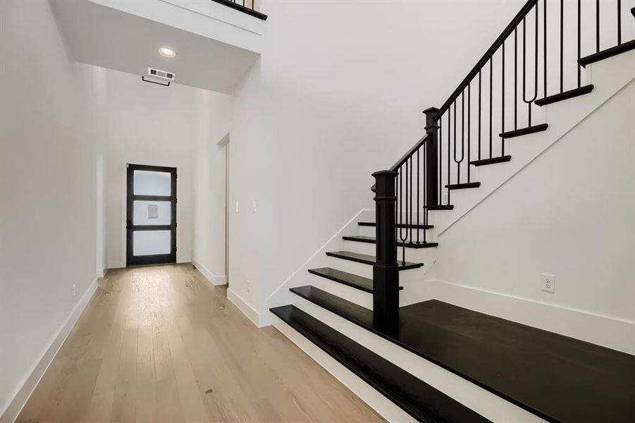 Entryway featuring a modern front door with frosted glass panels, light wood-finish flooring, a contemporary staircase with black risers and wrought iron balusters, and recessed ceiling lighting Entryway featuring a modern front door with frosted glass panels, light wood-finish flooring, a contemporary staircase with black risers and wrought iron balusters, and recessed ceiling lighting