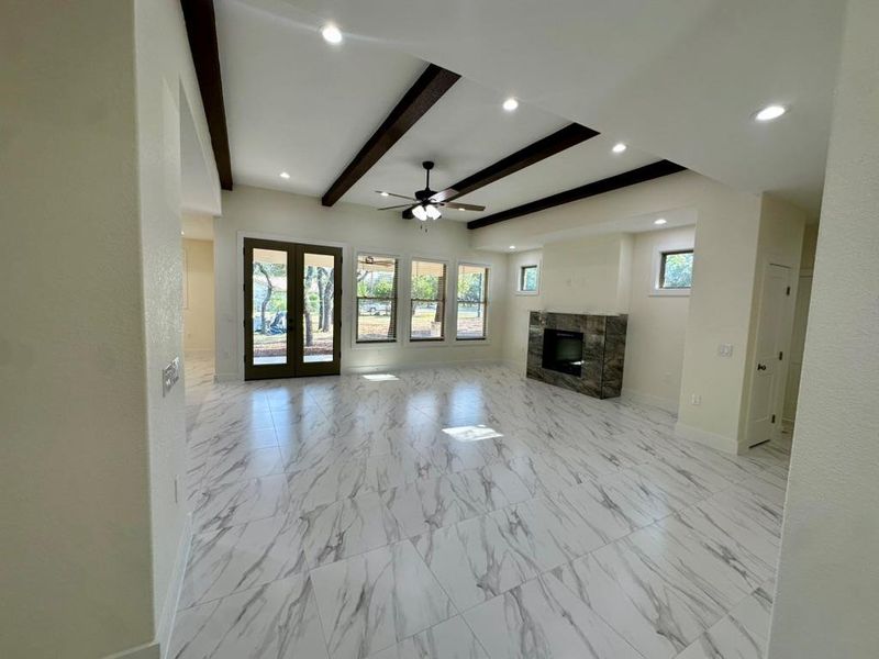 Unfurnished living room with beam ceiling, a high end fireplace, plenty of natural light, ceiling fan, and light marble finish floors