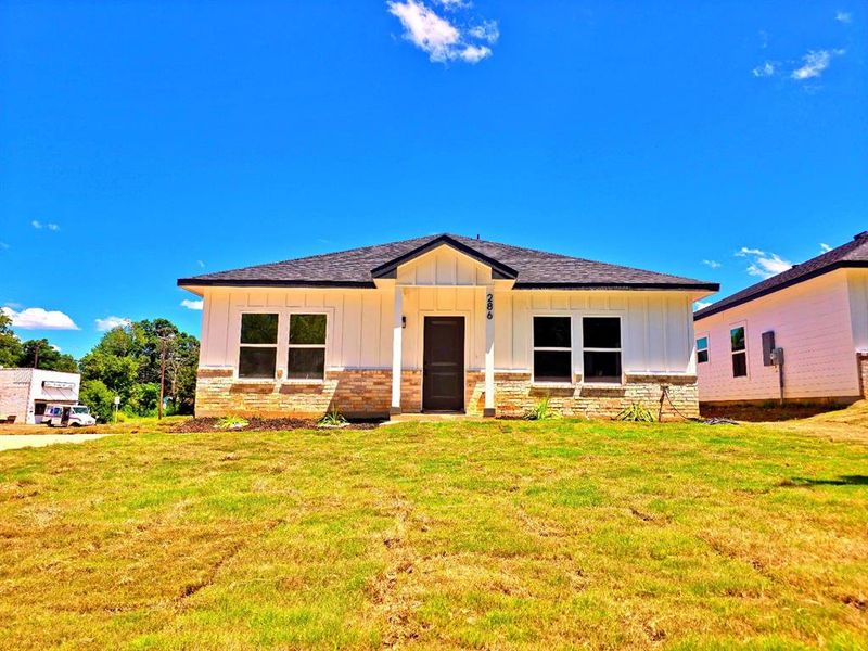 View of front of home with board and batten siding, a front yard, a porch, roof with shingles, and brick siding View of front of home with board and batten siding, a front yard, a porch, roof with shingles, and brick siding