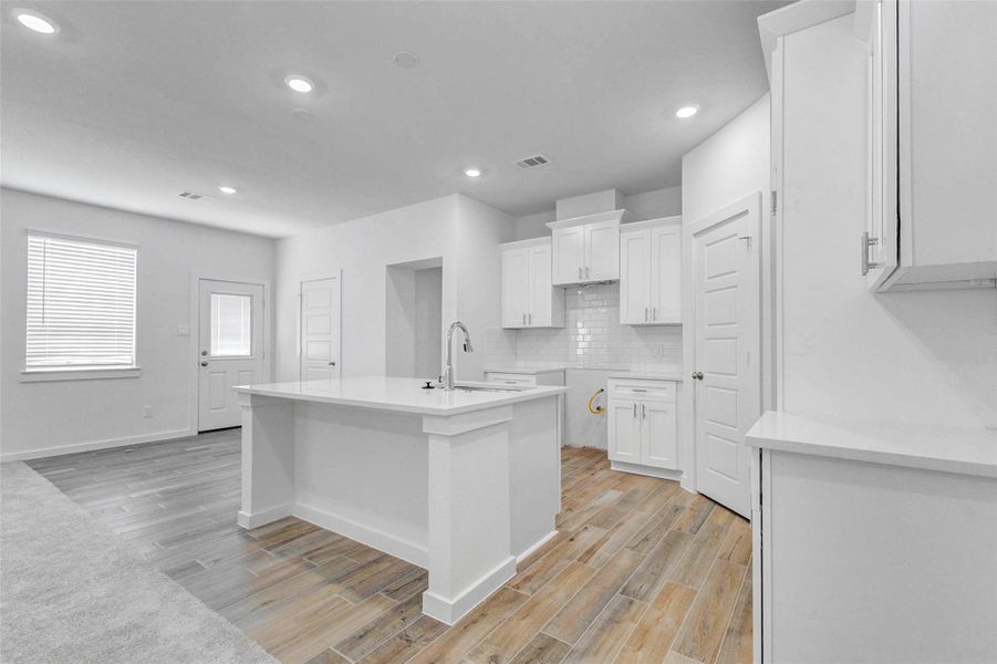Bright kitchen view featuring a large center island, white cabinetry, quartz-style countertops, subway tile backsplash, recessed lighting, and wood-look tile flooring. The open layout connects easily to the dining and living areas, creating a clean, functional space for meal prep, casual seating, and entertaining.
