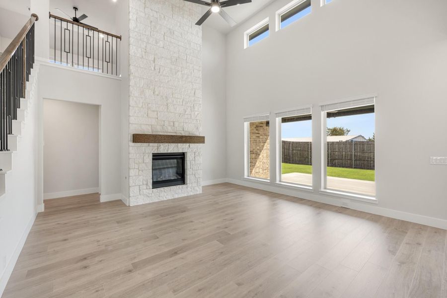 Open living room with two-story ceiling, stone fireplace, wood mantel, and hardwood floors Open living room with two-story ceiling, stone fireplace, wood mantel, and hardwood floors