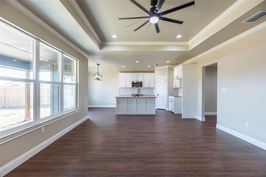 Expansive open-concept living area featuring wood-finish flooring, a tray ceiling with recessed lighting and a ceiling fan, and large windows