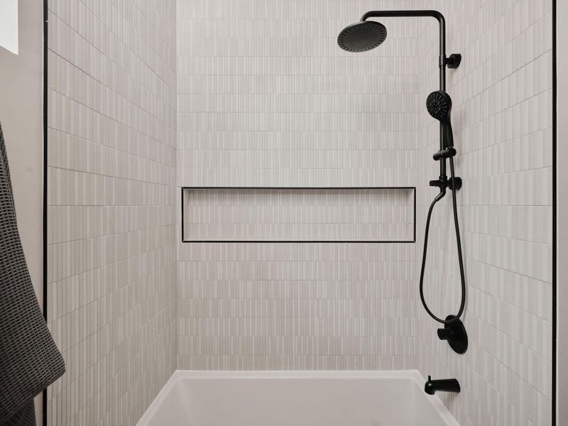 Tub and shower combination featuring floor-to-ceiling textured tile with a matte black shower system