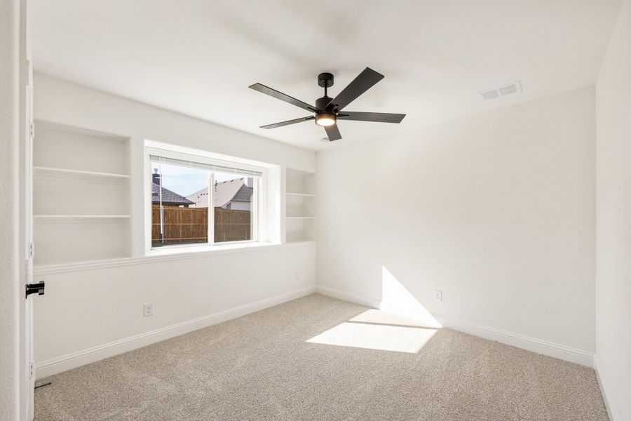 Empty bedroom with carpet flooring, black ceiling fan, built-in shelves, and a window with natural light