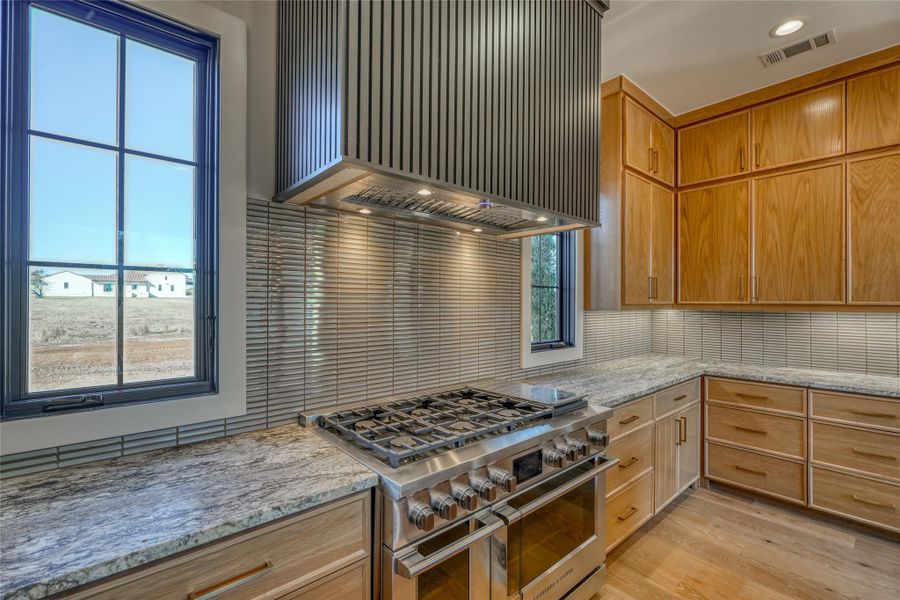 Beautiful custom range hood with tile backsplash & double oven & warming drawer.