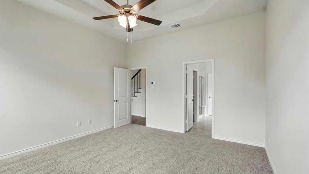 Spacious carpeted room featuring a tray ceiling with a ceiling fan, white paneled doors, and light-colored walls